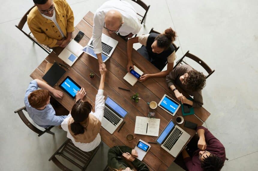 Top view of a diverse team collaborating in an office setting with laptops and tablets, promoting cooperation.